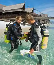 PADI instructor conducting a dive course in the shallow, clear waters of Mataking Island, with the luxury resort in the background.
