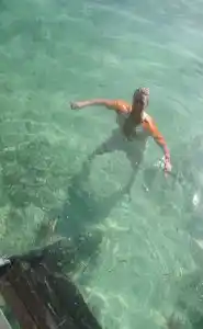 Passez directement de votre chambre à la mer rafraîchissante. Un client marche dans l'eau claire et peu profonde directement accessible depuis la longhouse du Mabul Backpackers, parfait pour une baignade rafraîchissante.