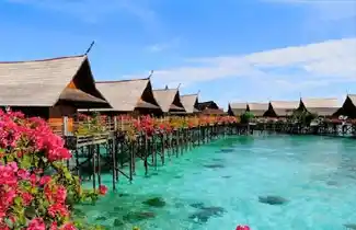 Vibrant bougainvillea flowers adorning the walkways of Kapalai Resort's overwater chalets, with a stunning view towards Mabul Island.