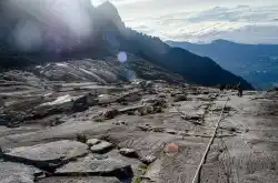 The rope section is a key part of the final ascent. Climbers using the guide rope to ascend the bare granite summit plateau of Mount Kinabalu on their way to the peak.