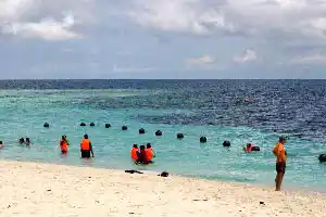 Snorkeling is a great way to see the shallow reefs. Snorkelers in bright orange vests float above the shallow reef off the Sipadan jetty enjoying calm turquoise sea under cloudy skies.