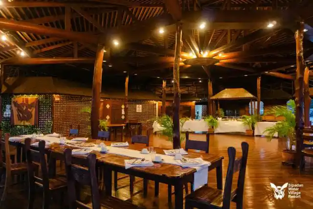 Le restaurant élégant du Sipadan Water Village, bâti en bois, avec ses tables chaleureusement éclairées et dressées pour le dîner.