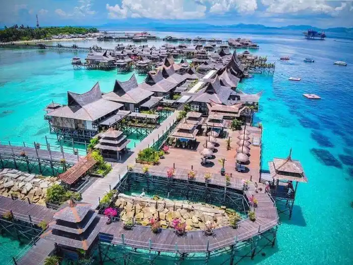 See the full scale and beauty of this water village. Spectacular aerial drone view of the entire Mabul Water Bungalows resort, its intricate network of jetties, and the surrounding turquoise Celebes Sea.
