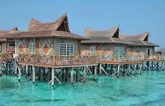 Your beautifully designed private bungalow awaits. Beautifully designed overwater bungalows at Mabul Water Bungalows resort, standing in the crystal-clear turquoise ocean on a sunny day.