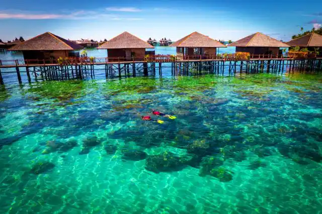 Snorkel the lively reef right outside your chalet. Snorkelers exploring the lively coral reef in crystal-clear turquoise water directly in front of the overwater chalets at Sipadan Water Village.
