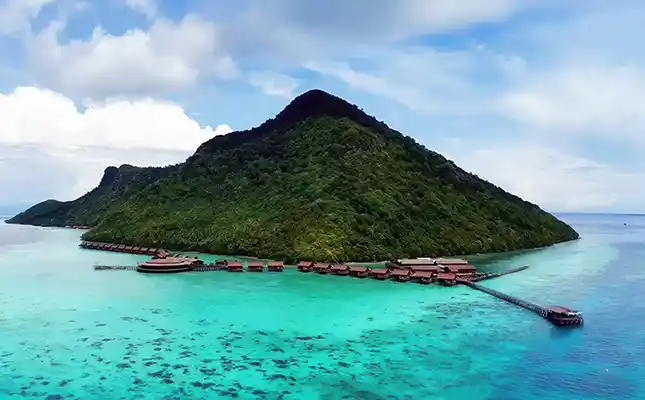 Wake up to the beauty of a volcanic island lagoon. Stunning aerial view of the Bohey Dulang Resort (Pearl Island Resort) with its overwater chalets nestled in a turquoise bay at the foot of a lush, volcanic island.
